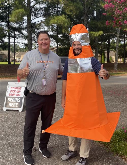 Board member Tim Holtcamp dressed as traffic cone beside principal  at Liberty Middle